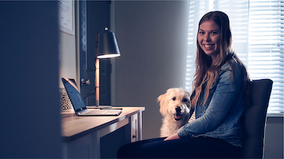 Military spouse works remotely from a computer in her home office as her dog sits nearby